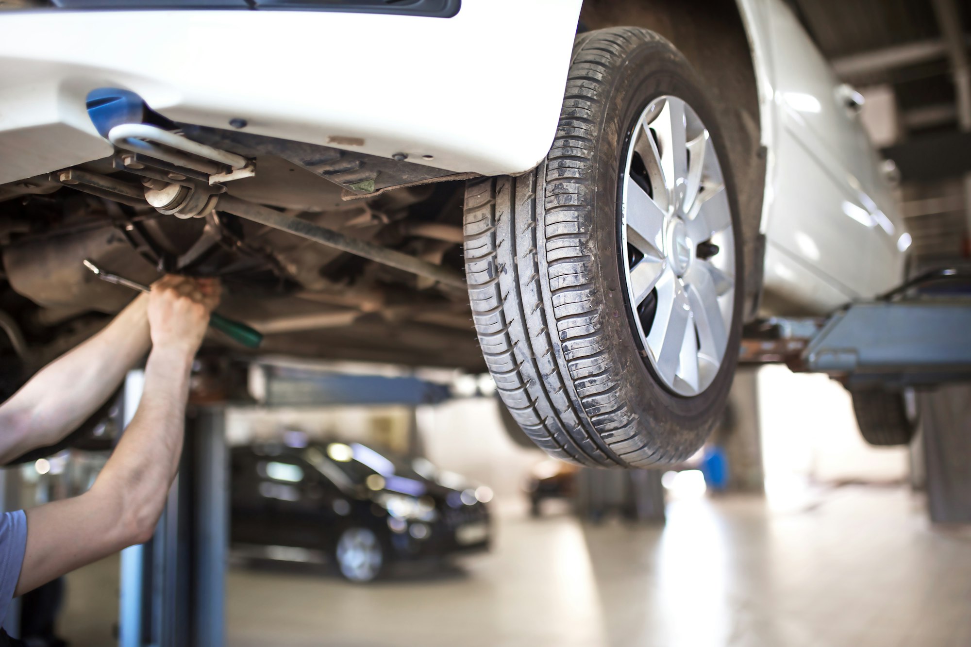 The car is lifted for repair on a lift in a car service station, a mechanic in overalls repairs